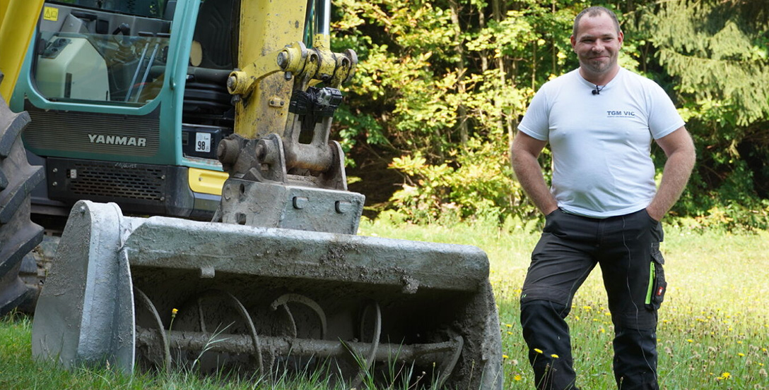20 Year Testimony TGM Vic Man standing next to Yanmar excavator which has a Modularis Drive Concrete Mixing Bucket attached to it.