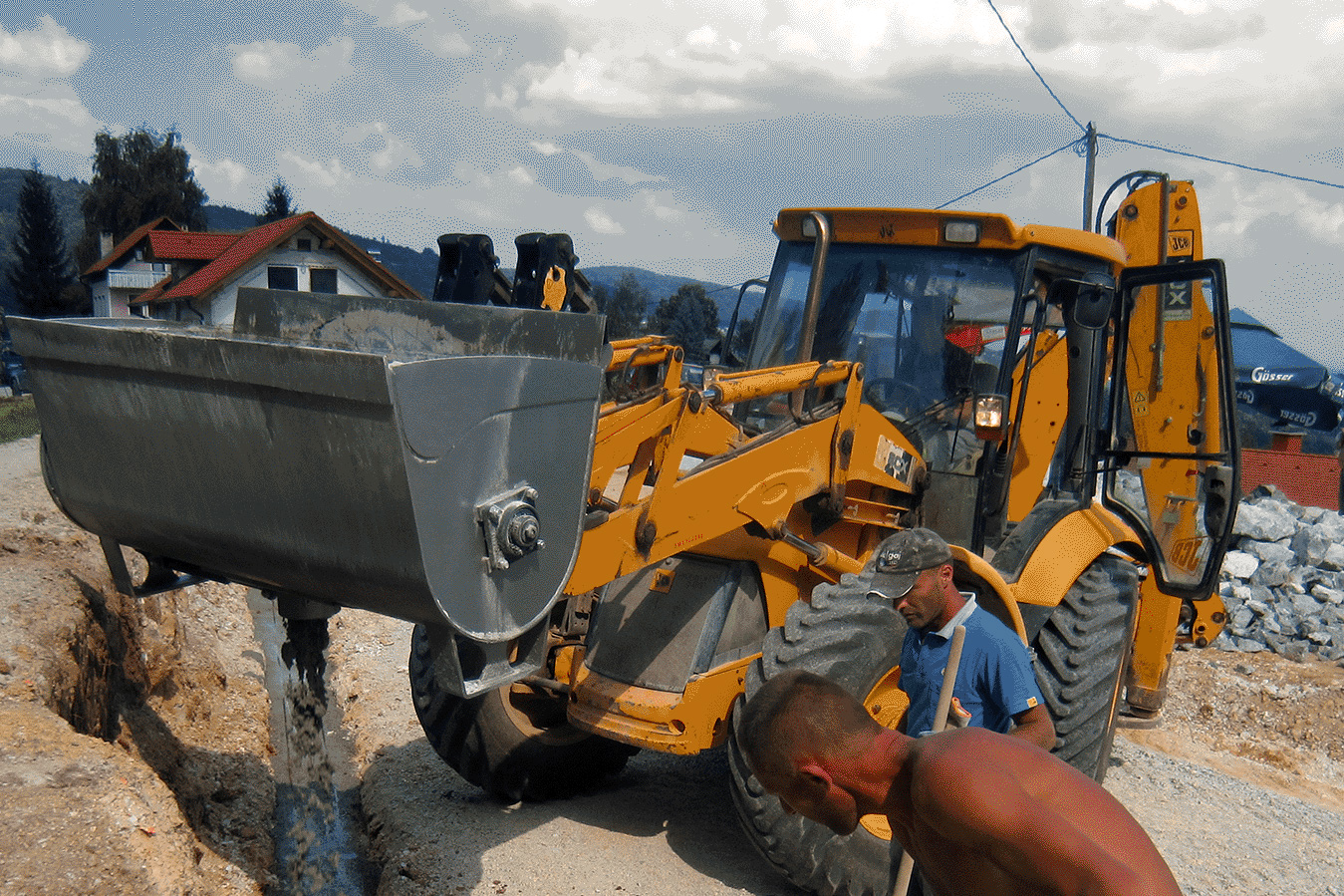 MMB600L JCB 4CX Modularis Drive 600 liter loader version concrete mixing bucket attached to JCB 4CX backhoe loader. Two construction workers beside the heavy machinery on the construction site.